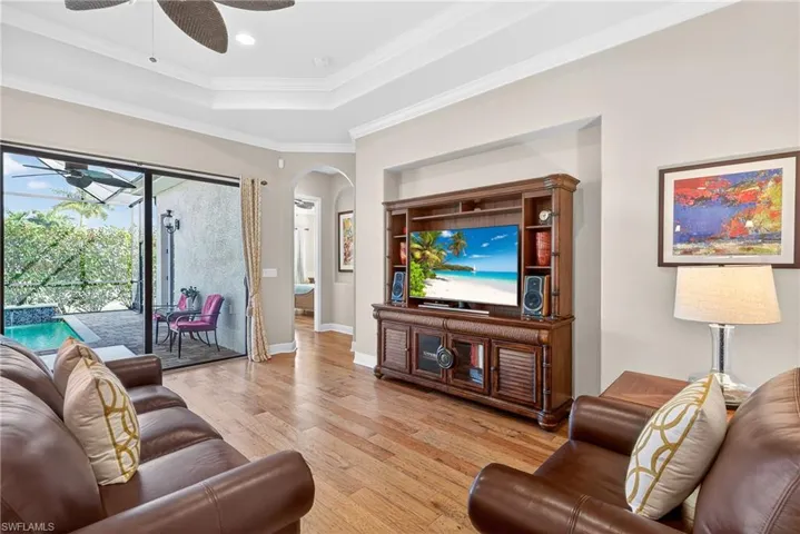 Living area with tray ceiling, crown molding, ceiling fan, engineered hardwood floors, and impact sliding glass doors opening to the covered lanai and pool