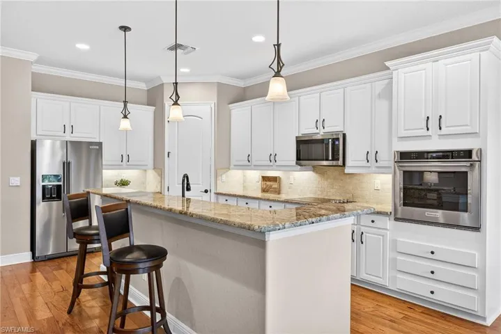 Open-concept kitchen with white cabinetry, breakfast bar seating, stainless steel appliances