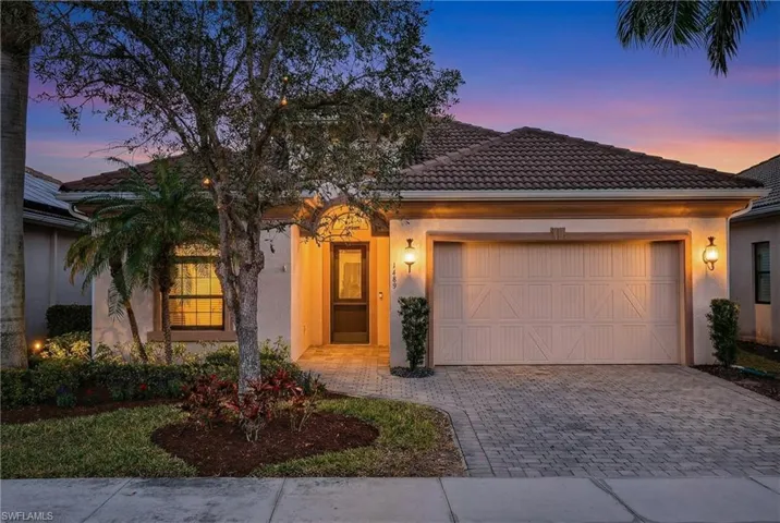 Naples Florida pool home at sunset with two-car garage, paver driveway, tile roof, and manicured landscaping in preferred X500 flood zone