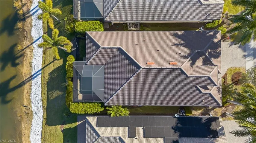 Aerial view of lakefront Naples pool home in X500 no flood zone featuring heated pool, southwestern exposure, and seamless indoor-outdoor living in a gated community