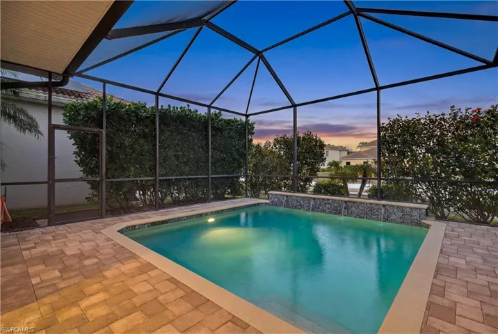 Southwestern-exposure screened lanai at sunset featuring heated pool, water features, lake views, and enhanced tropical landscaping for privacy