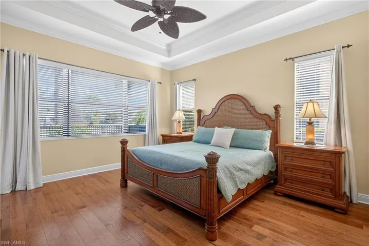 Bedroom with engineered hardwood flooring, crown molding, tray ceiling, a ceiling fan, and lake views