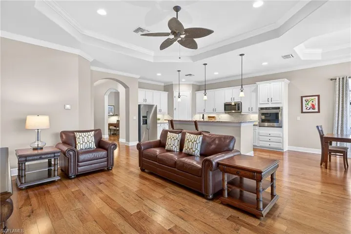 Open-concept living area with tray ceiling, crown molding, hardwood floors, and direct flow into adjacent kitchen
