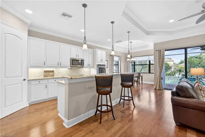 Open-concept kitchen with white cabinetry, breakfast bar seating, stainless steel Kitchen-Aid and Bosch appliances, and direct access to lanai, and impact glass doors to lanai