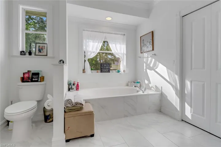 Full bath featuring baseboards, toilet, a bath, and marble finish floor