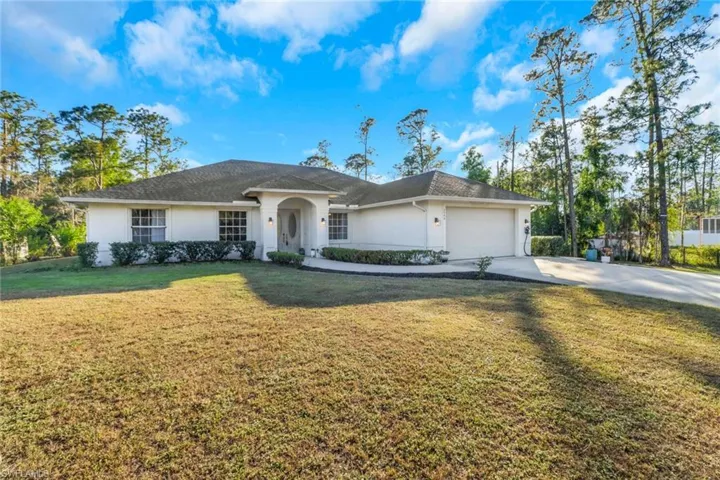 Ranch-style house with a garage, driveway, a front yard, and stucco siding