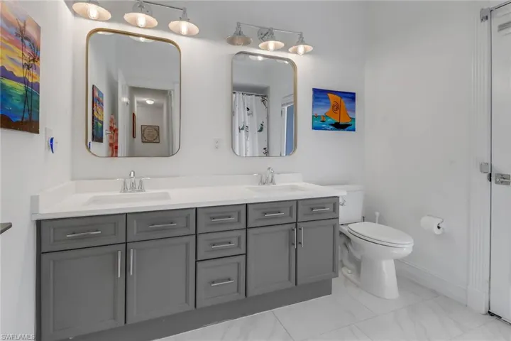 Bathroom with double vanity, a sink, marble finish floor, and toilet