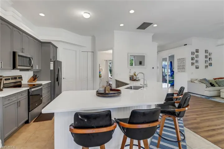 Kitchen featuring light tile patterned flooring, a sink, stainless steel appliances, gray cabinetry, and ornamental molding
