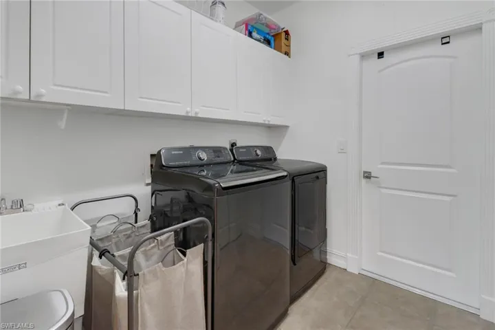 Laundry area featuring a sink, light tile patterned flooring, cabinet space, and washing machine and clothes dryer
