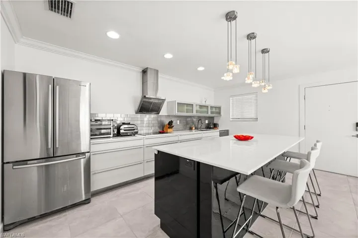 Dual tone kitchen featuring freestanding refrigerator, a breakfast bar, ornamental molding, pendant lighting, and glass fronted cabinets