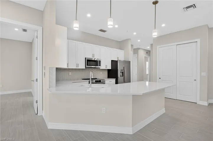 Kitchen with a peninsula, white cabinets, stainless steel appliances, and hanging light fixtures