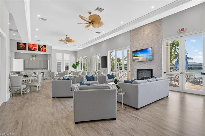 Living room with french doors, light wood-type flooring, a ceiling fan, a large fireplace, and a high ceiling