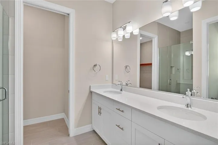 Bathroom with a stall shower, double vanity, a spacious closet, and wood finish floors