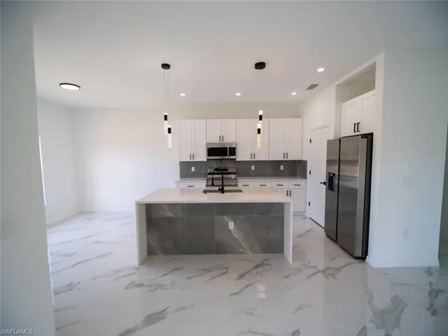 Kitchen featuring appliances with stainless steel finishes, a center island with sink, pendant lighting, light stone countertops, and backsplash