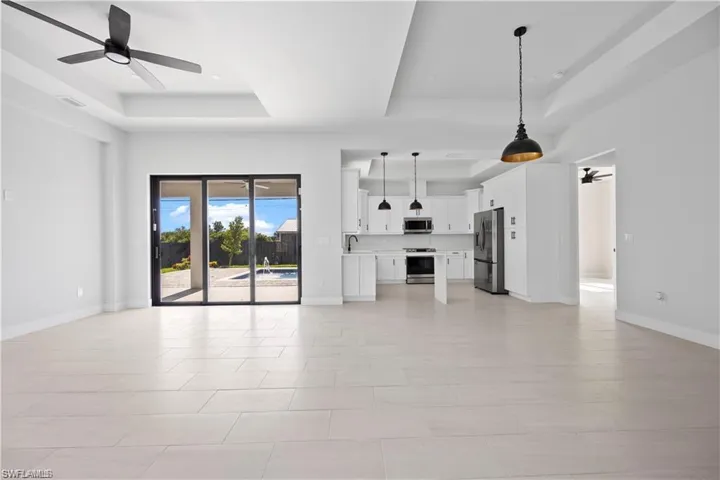 Unfurnished living room with baseboards, a raised ceiling, ceiling fan, and a sink