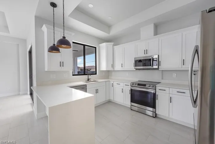 Kitchen with white cabinetry, stainless steel appliances, a peninsula, light countertops, and a raised ceiling