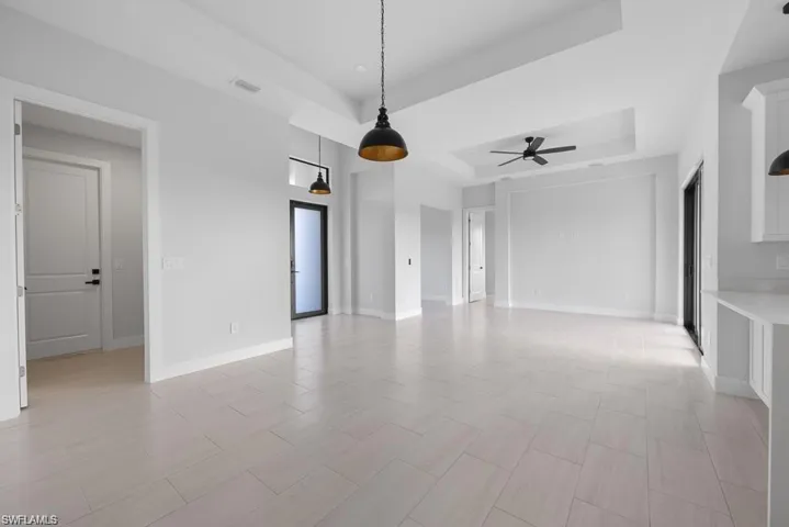 Empty room with a tray ceiling, baseboards, visible vents, and ceiling fan