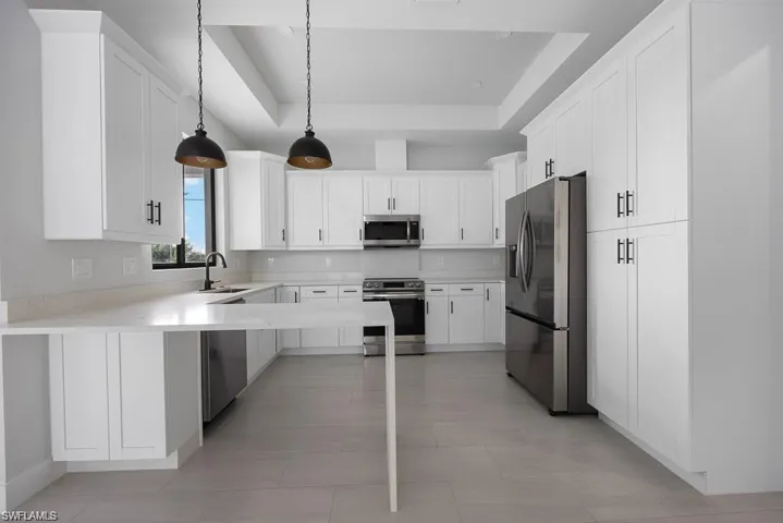 Kitchen featuring a sink, light countertops, white cabinets, appliances with stainless steel finishes, and a raised ceiling