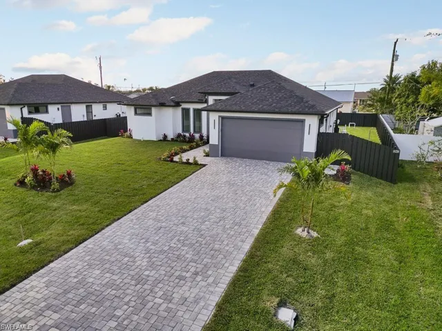 View of front of house featuring stucco siding, driveway, fence, a front yard, and a garage