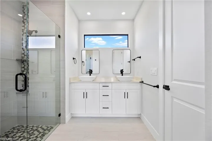 Full bath featuring double vanity, a shower stall, baseboards, and a sink