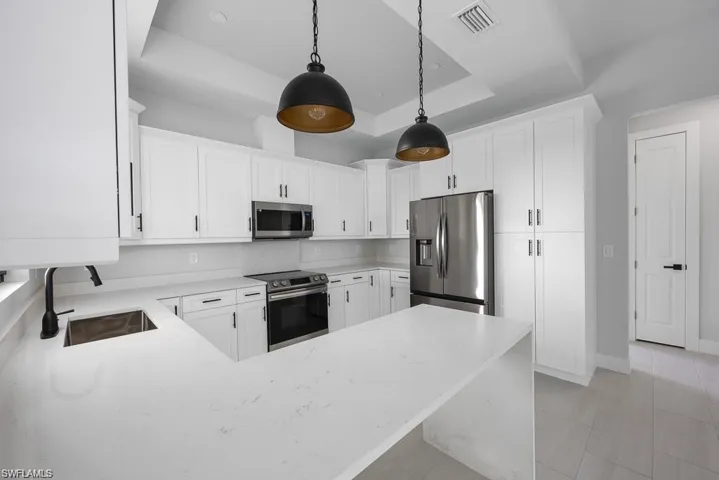 Kitchen with visible vents, hanging light fixtures, stainless steel appliances, a raised ceiling, and a sink