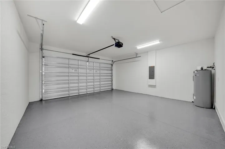Garage with water heater, electric panel, and a garage door opener