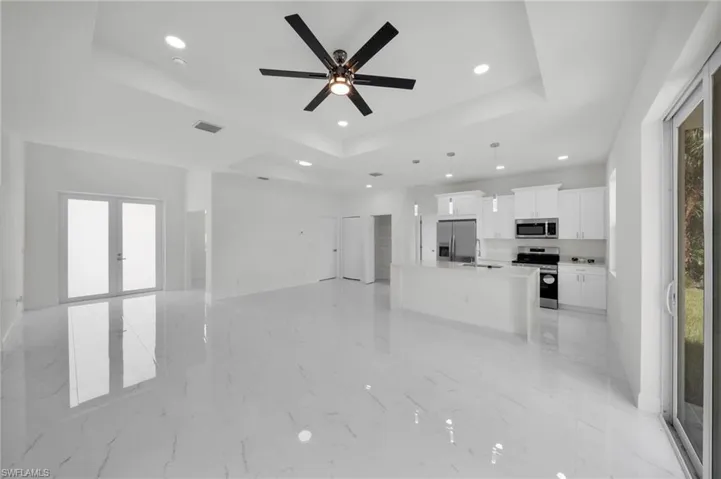 Unfurnished living room featuring a tray ceiling, plenty of natural light, recessed lighting, a ceiling fan, and french doors