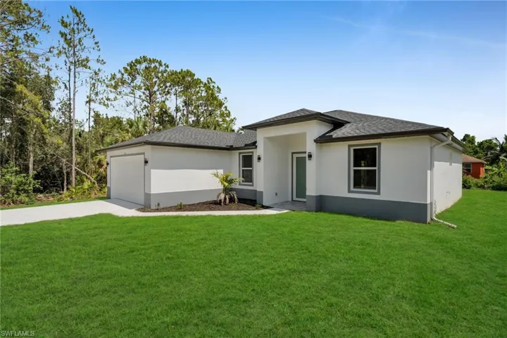 Prairie-style home with driveway, stucco siding, a front lawn, an attached garage, and roof with shingles
