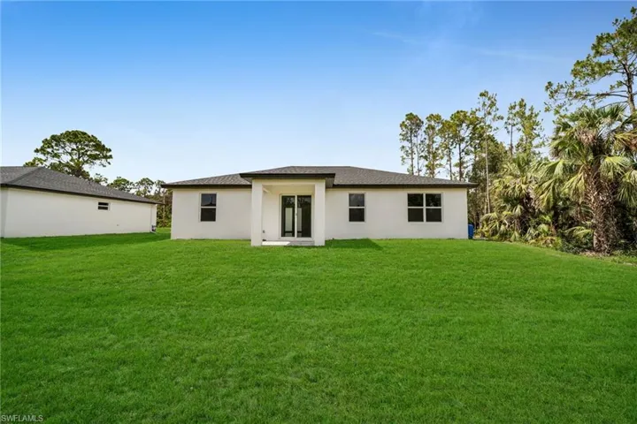 Rear view of house featuring a lawn and stucco siding