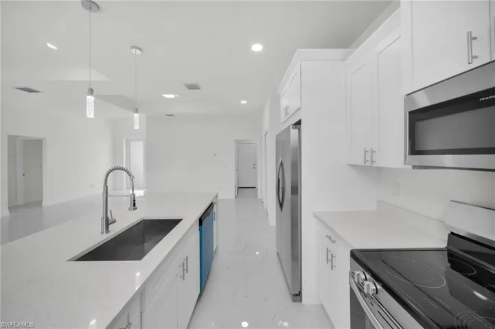 Kitchen with appliances with stainless steel finishes, white cabinetry, recessed lighting, decorative light fixtures, and light stone countertops