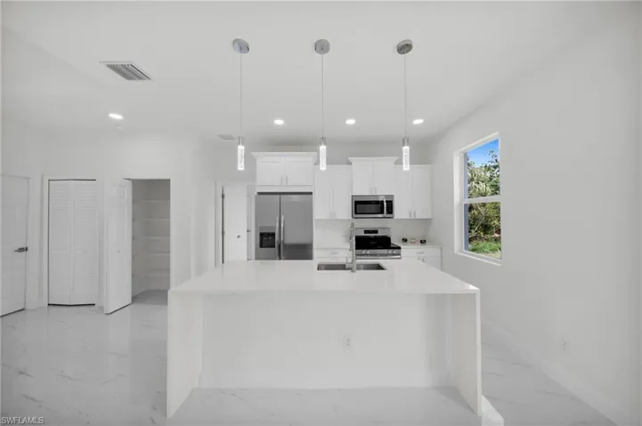 Kitchen featuring appliances with stainless steel finishes, light marble finish floors, white cabinetry, light countertops, and a kitchen island with sink