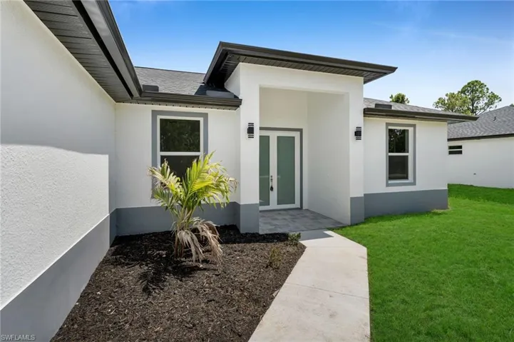 Entrance to property with french doors, stucco siding, a lawn, and roof with shingles