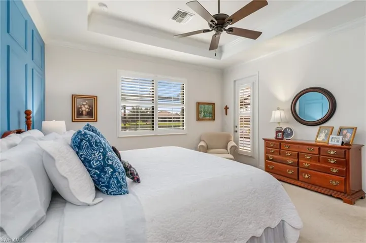 Carpeted bedroom featuring a tray ceiling, ornamental molding, and ceiling fan