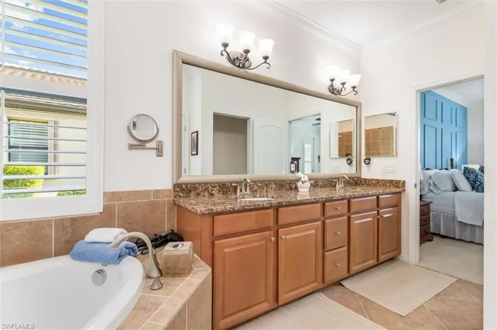Bathroom featuring double vanity, a garden tub, ensuite bathroom, light tile patterned floors, and crown molding