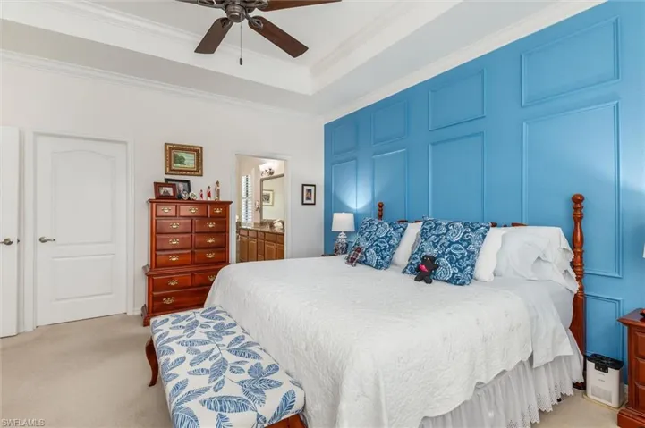 Bedroom with light carpet, crown molding, a ceiling fan, ensuite bathroom, and a tray ceiling