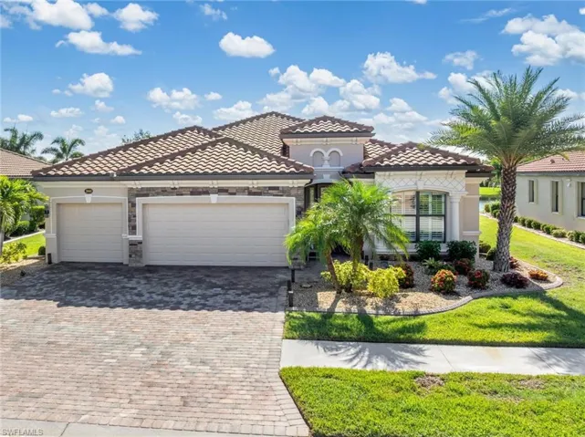 Mediterranean / spanish house with an attached garage, decorative driveway, a tiled roof, stone siding, and a front lawn