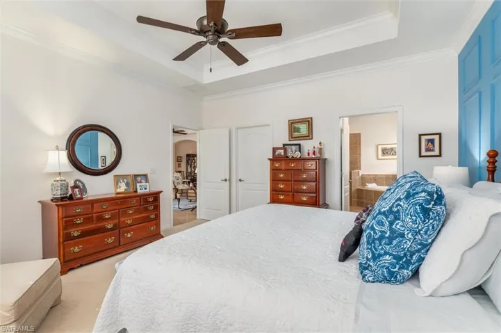Carpeted bedroom featuring a tray ceiling, arched walkways, a ceiling fan, crown molding, and connected bathroom