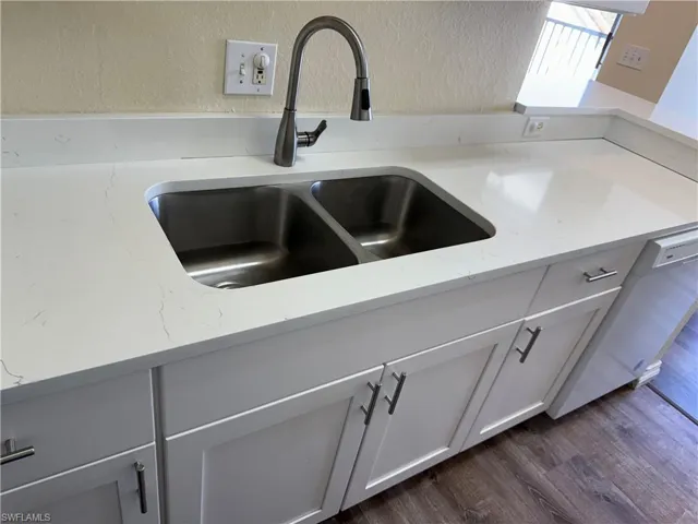 Kitchen view of a textured wall, white cabinetry, light stone countertops, dishwasher, and dark wood-style flooring