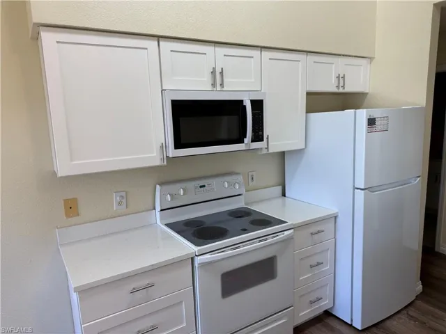 Kitchen featuring white appliances, white cabinetry, a textured wall, and dark wood-type flooring