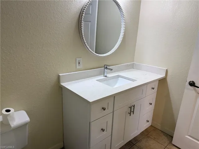 Half bath featuring a textured wall, vanity, and light tile patterned flooring