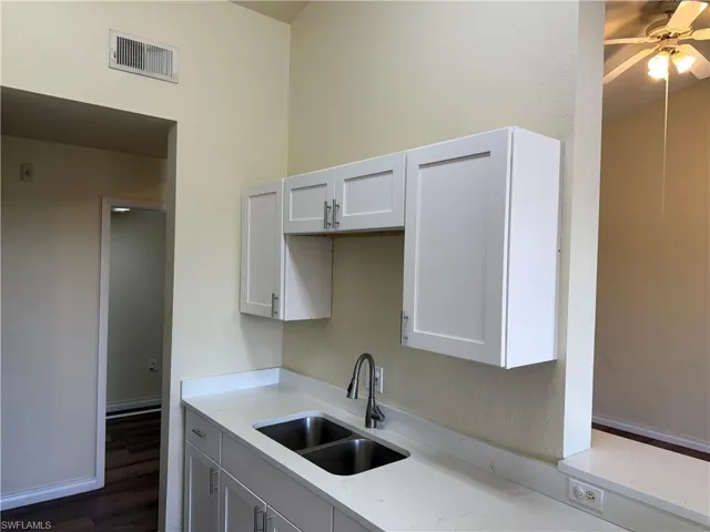 Kitchen with white cabinets, light stone countertops, and dark wood-type flooring