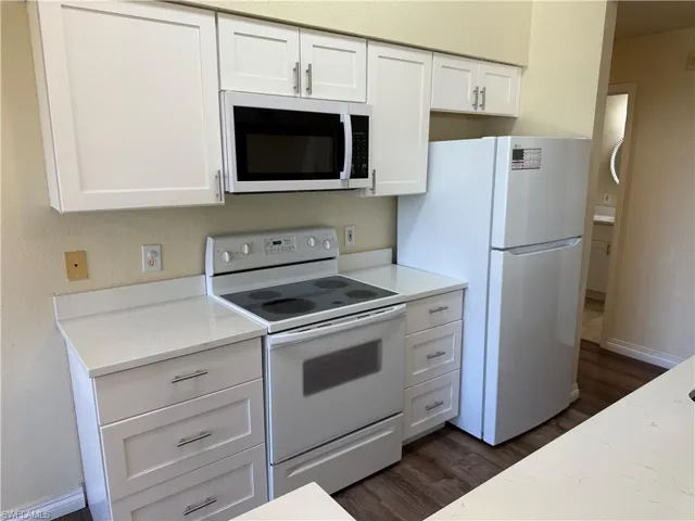 Kitchen with white appliances, white cabinets, dark wood finished floors, a textured wall, and light stone countertops