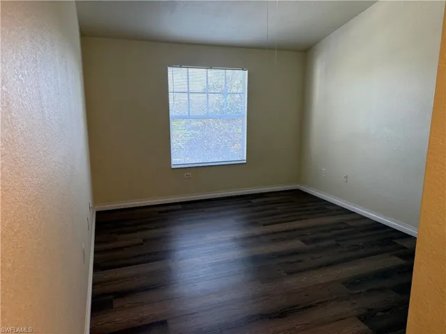 Empty room with a textured wall, dark wood-style floors, and a textured ceiling