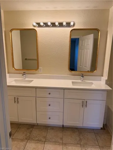 Full bath with double vanity, light tile patterned floors, and a textured wall