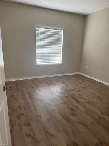 Room interior featuring wood-finish flooring, neutral wall paint, and a window with horizontal blinds