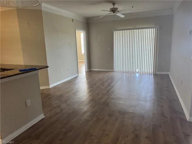 Open living area featuring wood-finish flooring, crown molding, a ceiling fan, and sliding glass doors with vertical blinds