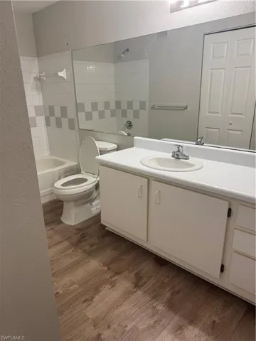 Bathroom featuring wood-finish flooring, a white vanity with an integrated sink, full-width wall mirror, and a tub with a tile surround