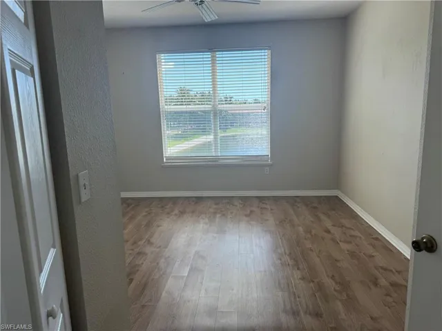 Room featuring wood-finish flooring, a ceiling fan, and a large window with horizontal blinds