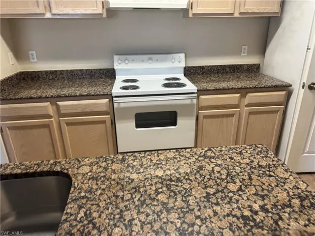 Kitchen featuring natural wood cabinetry, stone-patterned countertops, a white electric range, and an integrated stainless steel sink