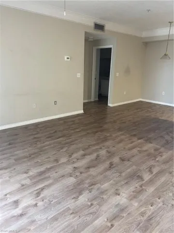 Neutral-toned interior space featuring wood-finish flooring, crown molding, and a suspended pendant light fixture